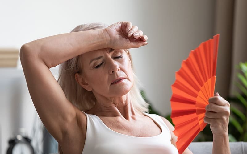 Mulher na menopausa sofrendo com ondas de calor, sintomas comuns que a amora miura pode ajudar a aliviar