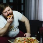 homem obeso comendo pizza no sofá