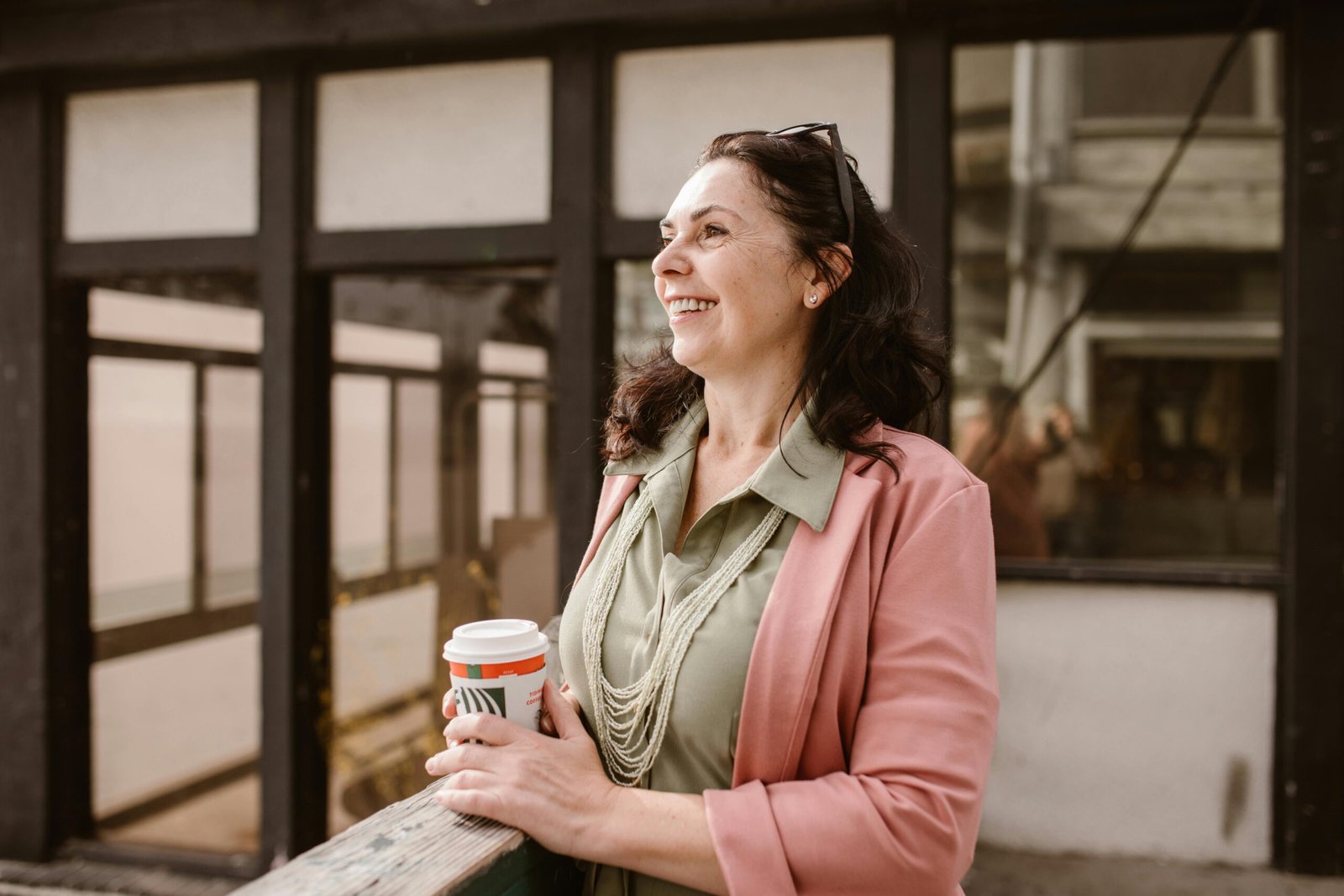 Uma mulher de meia-idade, sorridente e relaxada, segura uma xícara de café enquanto aproveita seu momento. Ela parece tranquila, simbolizando o alívio dos sintomas da menopausa, como ondas de calor e irritabilidade, após incluir o suplemento Amora Miura em sua rotina. A imagem transmite bem-estar e qualidade de vida.